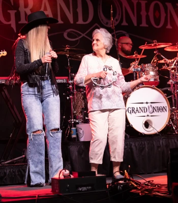 a woman holding a microphone next to a woman playing drums