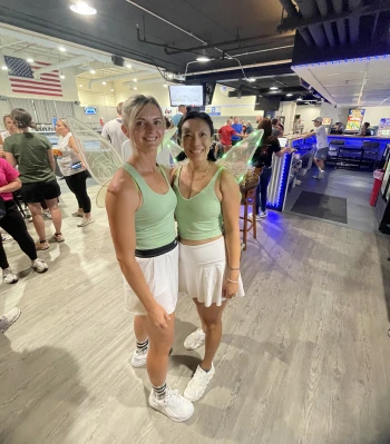 two women wearing fairy wings and standing in a room with people